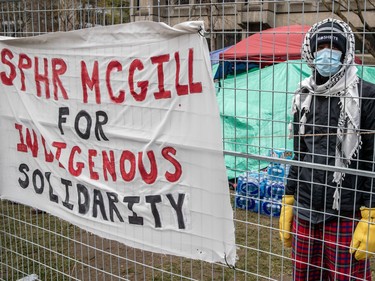 A person wearing a mask and kaffiyeh stands behind a fence where a sign reading 'SPHR McGill for Indigenous solidarity' is tied