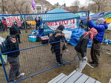 People wearing masks and scarves manipulate a temporary fence in an encampment