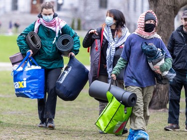 People wearing masks and scarves carry bags and rolled up mats along the grass