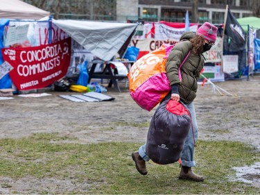 A woman carries two large bags walking away from a temporary fence with banners tied to it