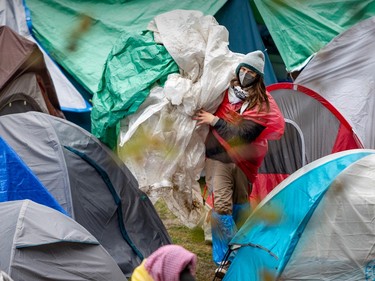 A man wearing several layers of clothing carries bundled-up tarps between camping tents