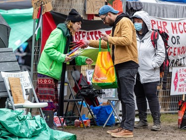 A man holds a reusable grocery bag and hands items from it to another person next to a temporary fence with banners attached to it