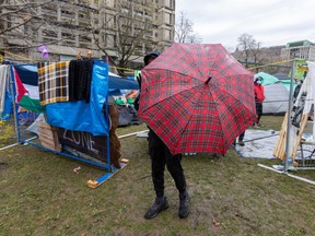 A man holds up an umbrella to block part of the view of an encampment on McGill's campus