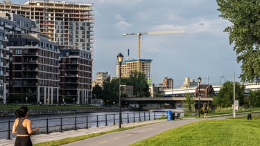 A woman dressed in a black workout set jogs along Montreal's Lachine Canal, with condo towers visible in the background and grass and the bike path visible in the foreground.