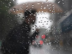A blurred person carrying an umbrella seen through a window covered in rain drops