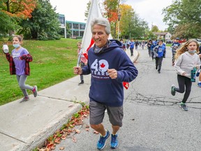 A man leads a marathon of children. He is smiling and wearing a sweatshirt that says 40 Years Marathon of Hope
