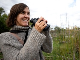 Katherine Collin holds a pair of binoculars while standing in wetlands