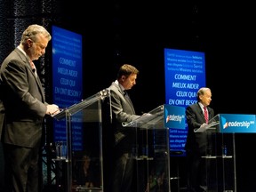 Three men stand at podiums set up debate-style