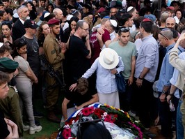 People gather packed tightly around a casket covered in flowers