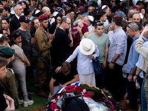 People gather packed tightly around a casket covered in flowers