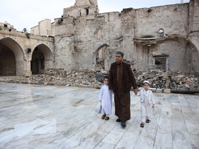 A Palestinian man walks with his kids on April 10, 2024 in rainy weather through the courtyard of Gaza City's historic Omari Mosque, which has been heavily damaged in Israeli bombardment during the ongoing battles between Israel and Hamas, after the morning prayer on the first day of Eid al-Fitr that marks the end of the Islamic fasting month of Ramadan.