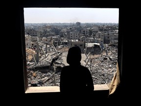 A Palestinian youth looks out of a window at buildings destroyed during Israeli bombardment in Khan Yunis, on the southern Gaza Strip on April 16, 2024, as fighting continues between Israel and the militant group Hamas.