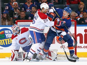 A Canadiens and Islanders player push up against each other while the Canadiens goalie looks off to the side
