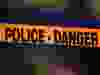 Police tape that says "police danger" in black on an orange ribbon, with a blurry background.