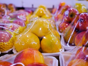 Assorted fresh fruits at the market stall are wrapped in plastic film to protect them.