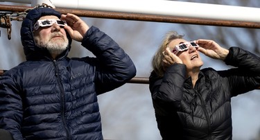 Two people wear eclipse glasses while looking up.