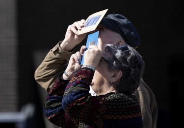 An older man and woman hold eclipse cards as they stare upward.