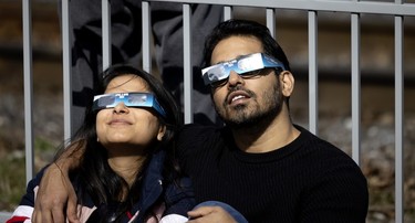 A woman and man wear eclipse glasses while looking at the sky.