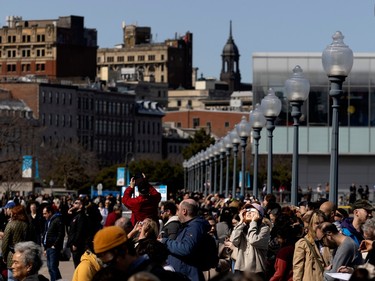 A crowd scene shows people in Montreal's Old Port as they watch the solar eclipse.