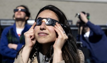 A woman presses eclipse glasses to her face.