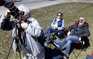 A man looks into his mounted camera with two people in the background as they wait for the solar eclipse.