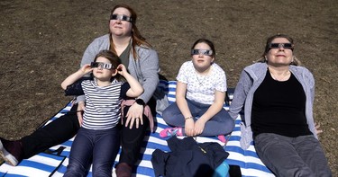 Vanessa Bissonnette, left, holds her daughter Rosalie Hamel as Marei-Sophie Hamel and grandmother Chantal Piche watch the solar eclipse in Montrea on Monday, April 8, 2024.