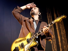 Singer Noah Kahan raises his hand to his eyes as he looks at his fans at the Bell Centre while holding a guitar.