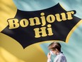 A person walks past a sign painted on a wall that reads "Bonjour Hi"