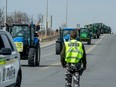 A police officer stands watch as a line of tractors parades down a two-lane road