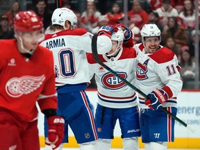 Three Canadiens celebrate on the ice while a Red Wings player looks unhappy