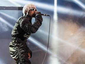 André 3000 is seen in a white wig and wearing sunglasses with white frames holding the mic up to his mouth as he performs at the Osheaga Music Festival at Jean-Drapeau Park in 2014.