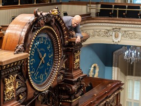 A man leans over to adjust a large clock
