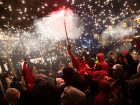 Participants dressed up as demons brandish sticks with fireworks on a street at night