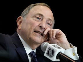 A close-up of NHL commissionar Gary Bettman, with his left hand on his face and speaknig into a microphone with the NHL logo on it.