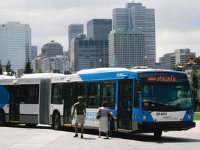Two people stand next to an articulated bus. The Montreal skyline is in the background.