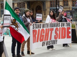 Protesters hold an Iranian flag, and signs reading Stand With Iranians on the Right Side of History and IRGC Terrorists.