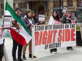 Protesters hold an Iranian flag, and signs reading Stand With Iranians on the Right Side of History and IRGC Terrorists.