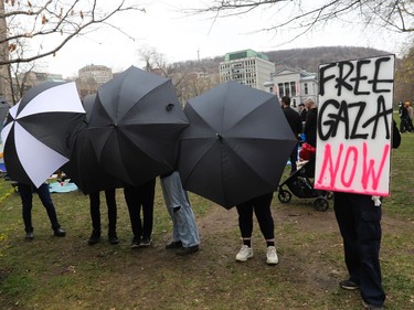 People use umbrellas to block the view while another person holds a spraypainted sign reading 'FREE GAZA NOW'