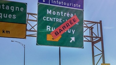 A highway sign showing the exit for Guy St. has an orange sticker saying barrée on top of it
