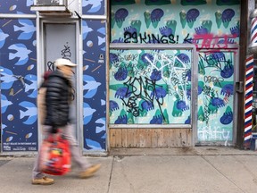 Pedestrians walks past closed shops with graffiti on them