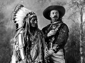 Sitting Bull and Buffalo Bill Cody pose together in front of a fake backdrop in 1885 in Montreal in a black and white image.