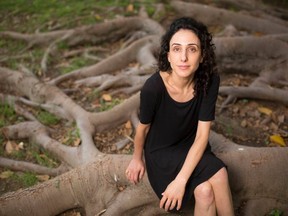A woman stares at the camera while sitting on the large roots of a tree.