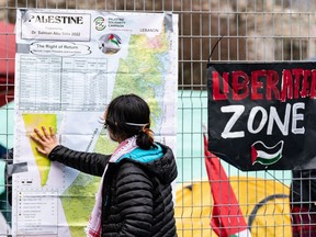 A pro-Palestinian activist looks at a map of Palestine taped to the fence around his camp on the McGill University campus in Montreal, Monday, April 29, 2024.