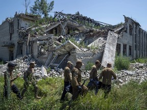 Oleksii Yukov, second right, and other body collectors carry the body of a Russian soldier that was exhumed from a shell crater in front of destroyed school in Virnopillia, Ukraine, Thursday, July 6, 2023.