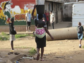 A woman carries a her baby and a bucket of water in Harare on April 6, 2020.