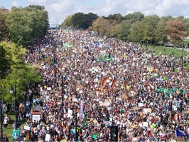A massive crowd marches for climate change in a green area.