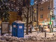 A portable toilet on a snowy city street corner.