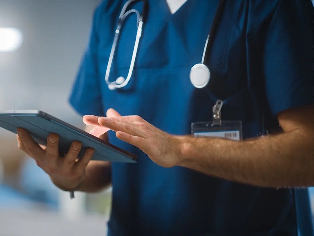A doctor seen from neck to waist works on a tablet.