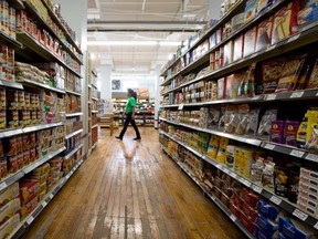 Grocery store aisles are seen on either side of this photo, with stocked shelves. An employee walks between the aisles in the background.