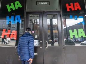A man looks through storefront doors. In the windows are giant colourful letters that say HA HA HA